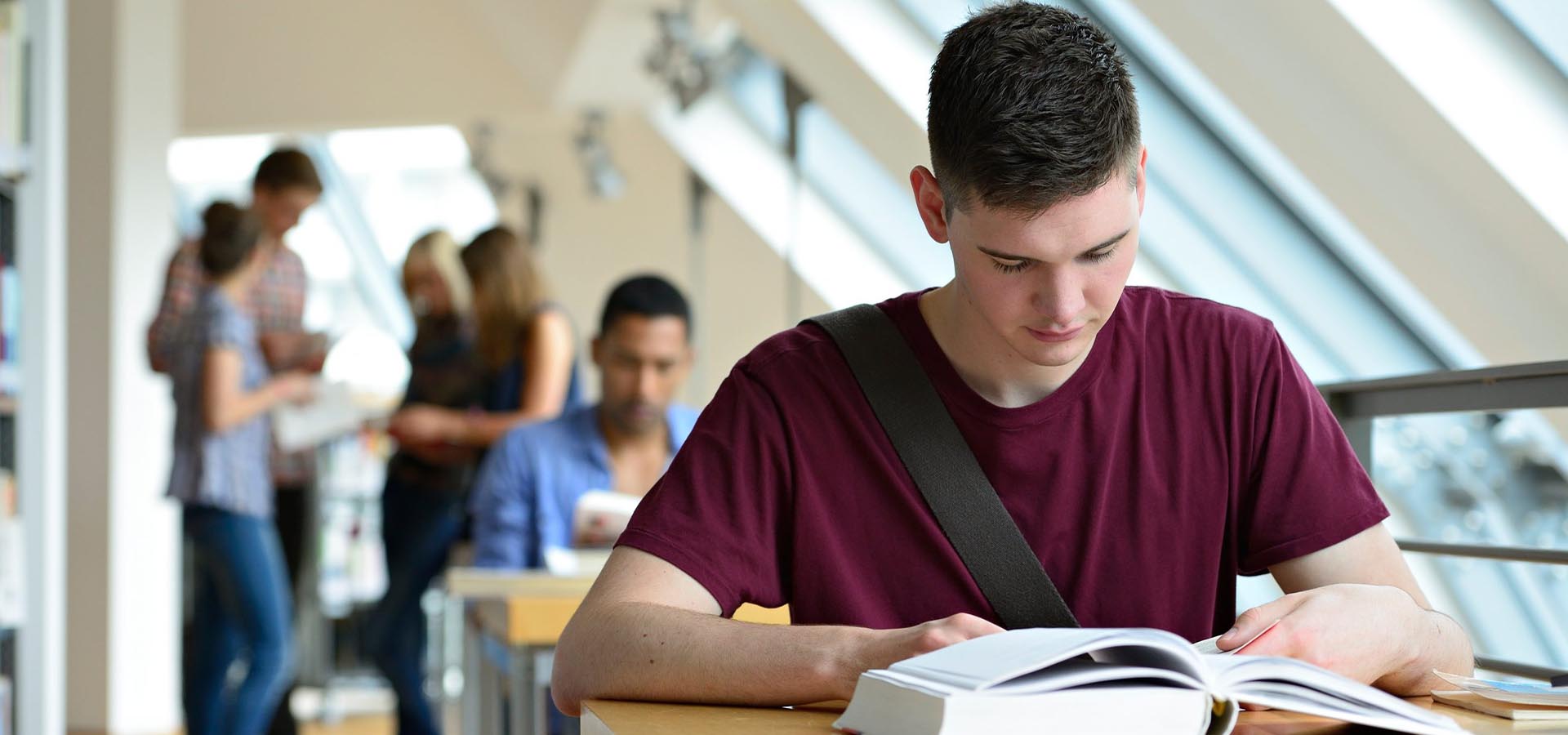 Student reading a textbook in a study area, representing focus and dedication in higher education.