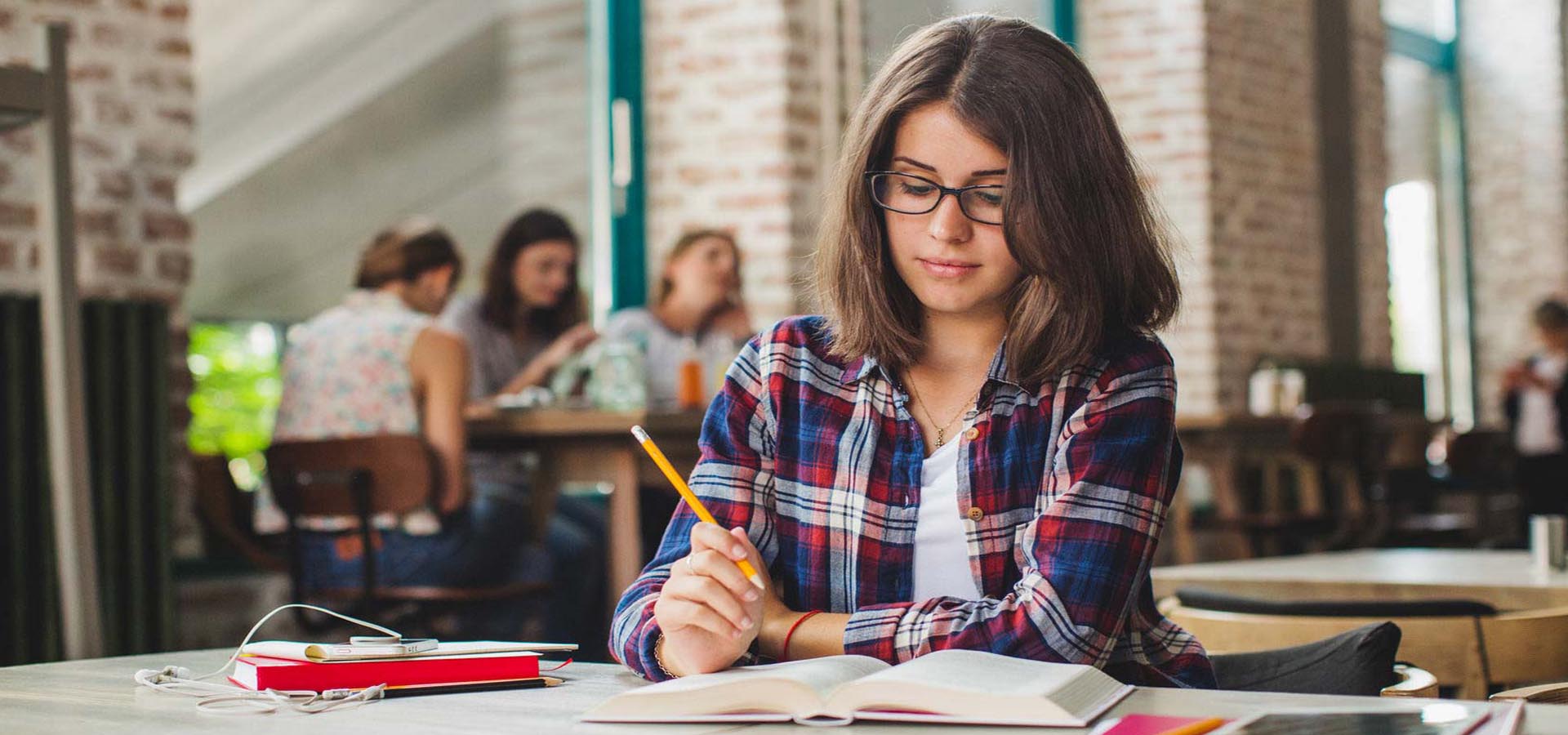 Student studying with a pencil and book in a cafe, representing independent learning in higher education.