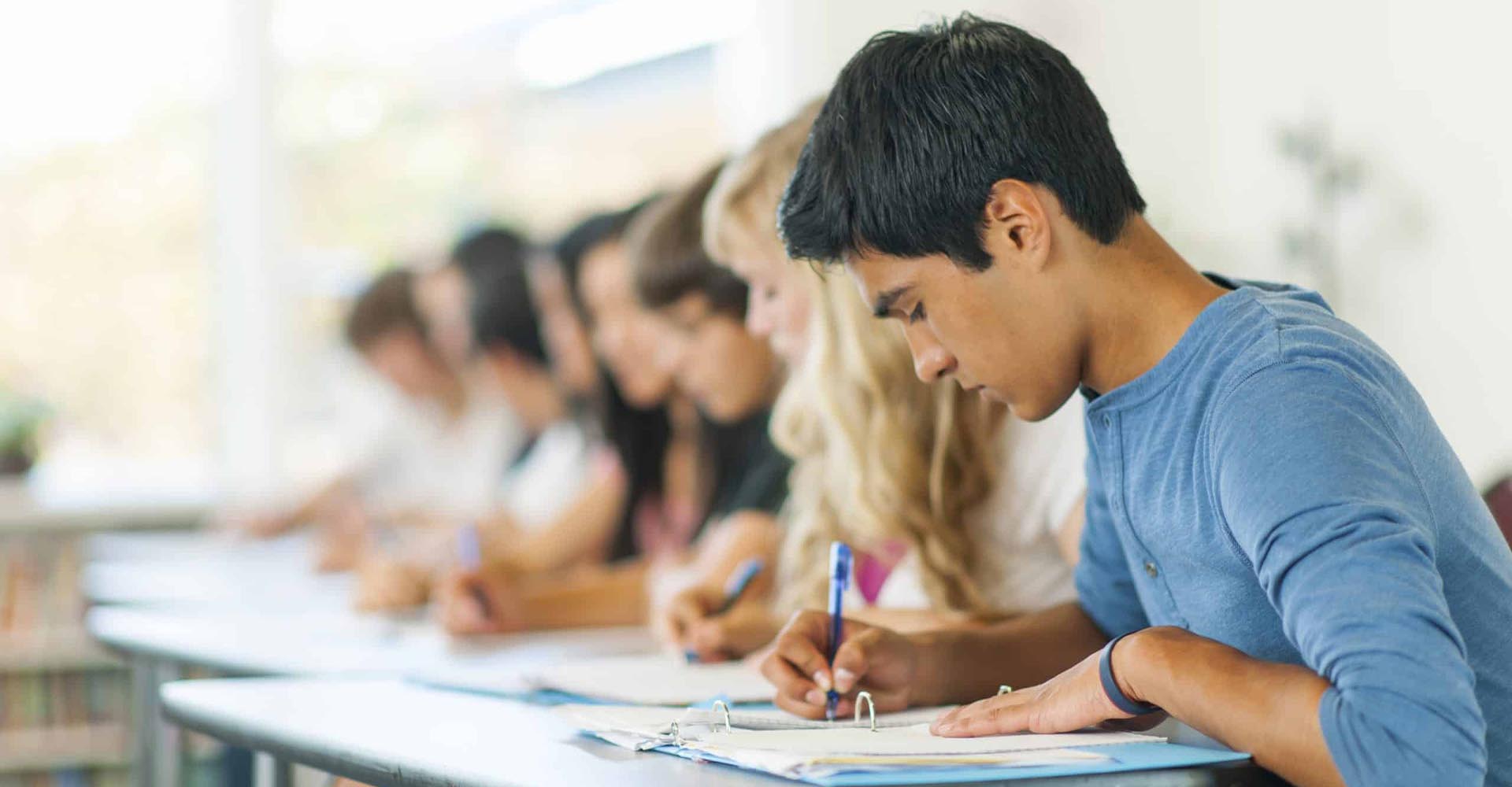 Students focused on writing in a classroom, representing the question