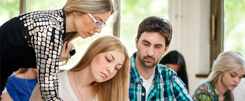 Instructor assisting students in a classroom, representing personalized guidance in pursuing a Bachelor Degree.
