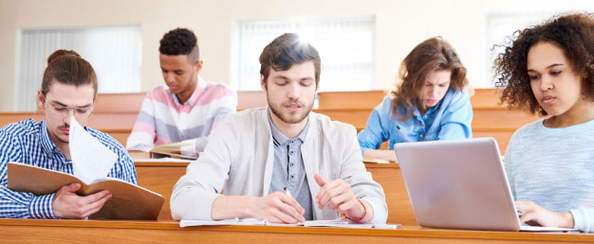 Students studying in a lecture hall with laptops and notes, representing coursework for a BTEC Higher National Diploma.