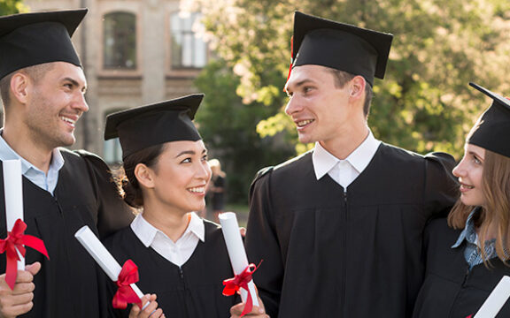 Four graduates in black caps and gowns holding diplomas, celebrating outdoors, representing the History and Evolution of HND courses achievements.