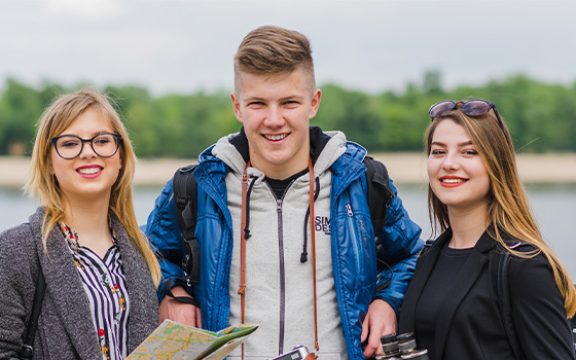Three smiling young adults by a body of water, possibly students, representing who should consider an HND program.