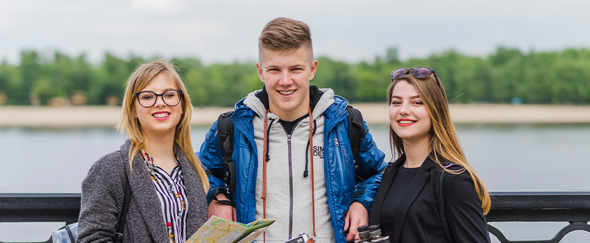 Three smiling young adults by a body of water, possibly students, representing who should consider an HND program.