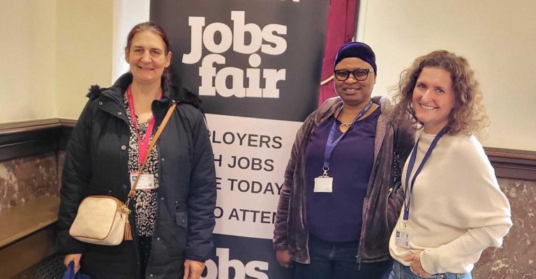 Three attendees posing in front of a banner at the Stratford Town Hall Jobs Fair.