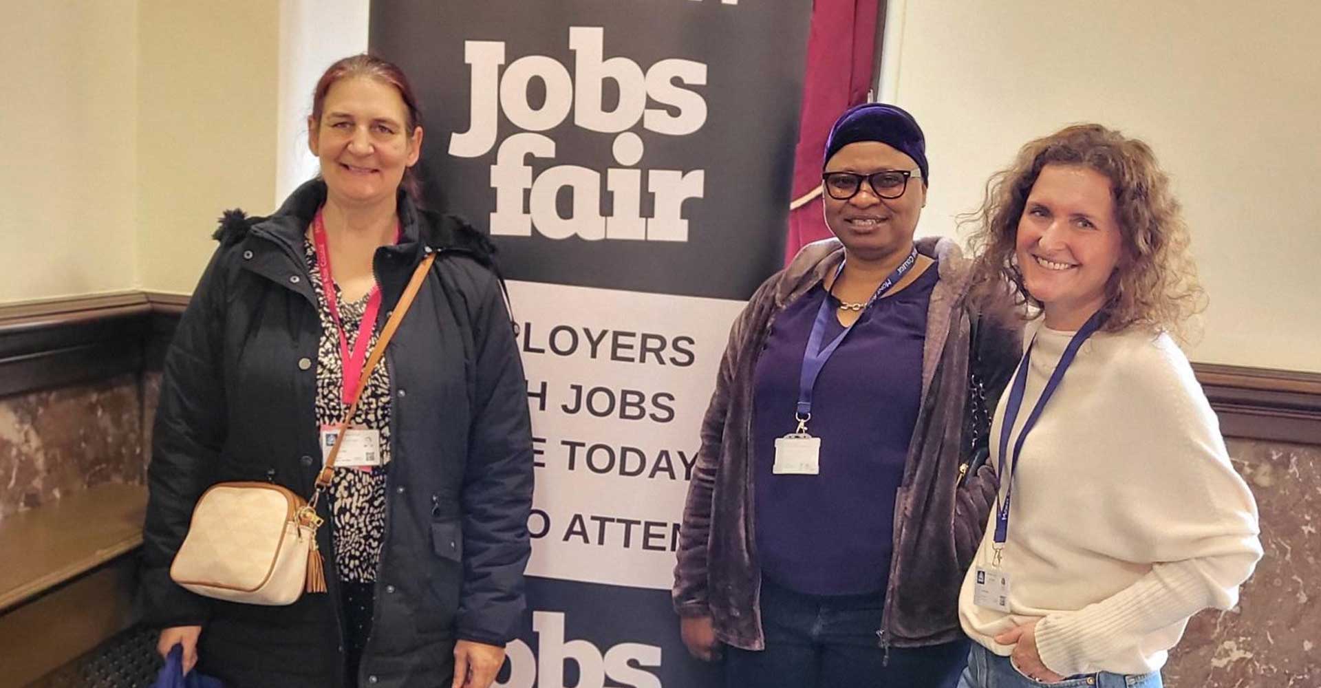 Three attendees posing in front of a banner at the Stratford Town Hall Jobs Fair.