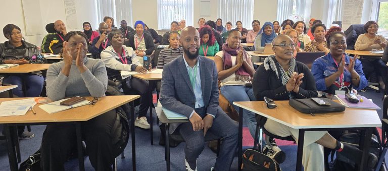 A diverse group of attendees in a classroom enthusiastically clapping during the Anthony Lindsay Black History Month Event at MRCollege.