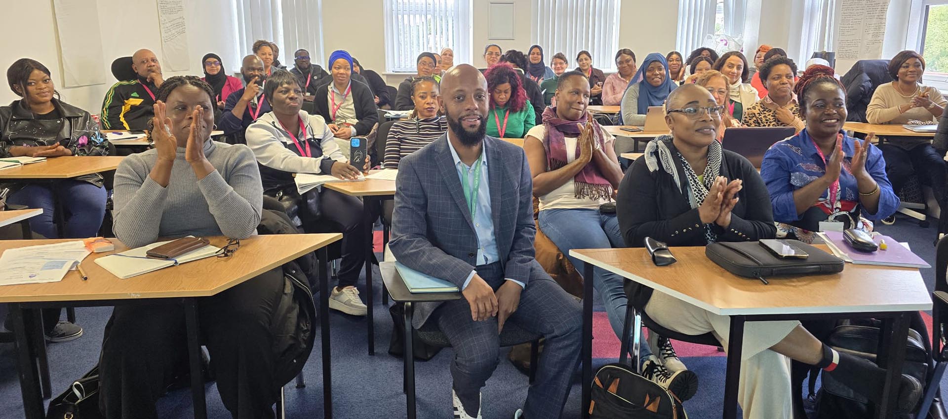 A diverse group of attendees in a classroom enthusiastically clapping during the Anthony Lindsay Black History Month Event at MRCollege.