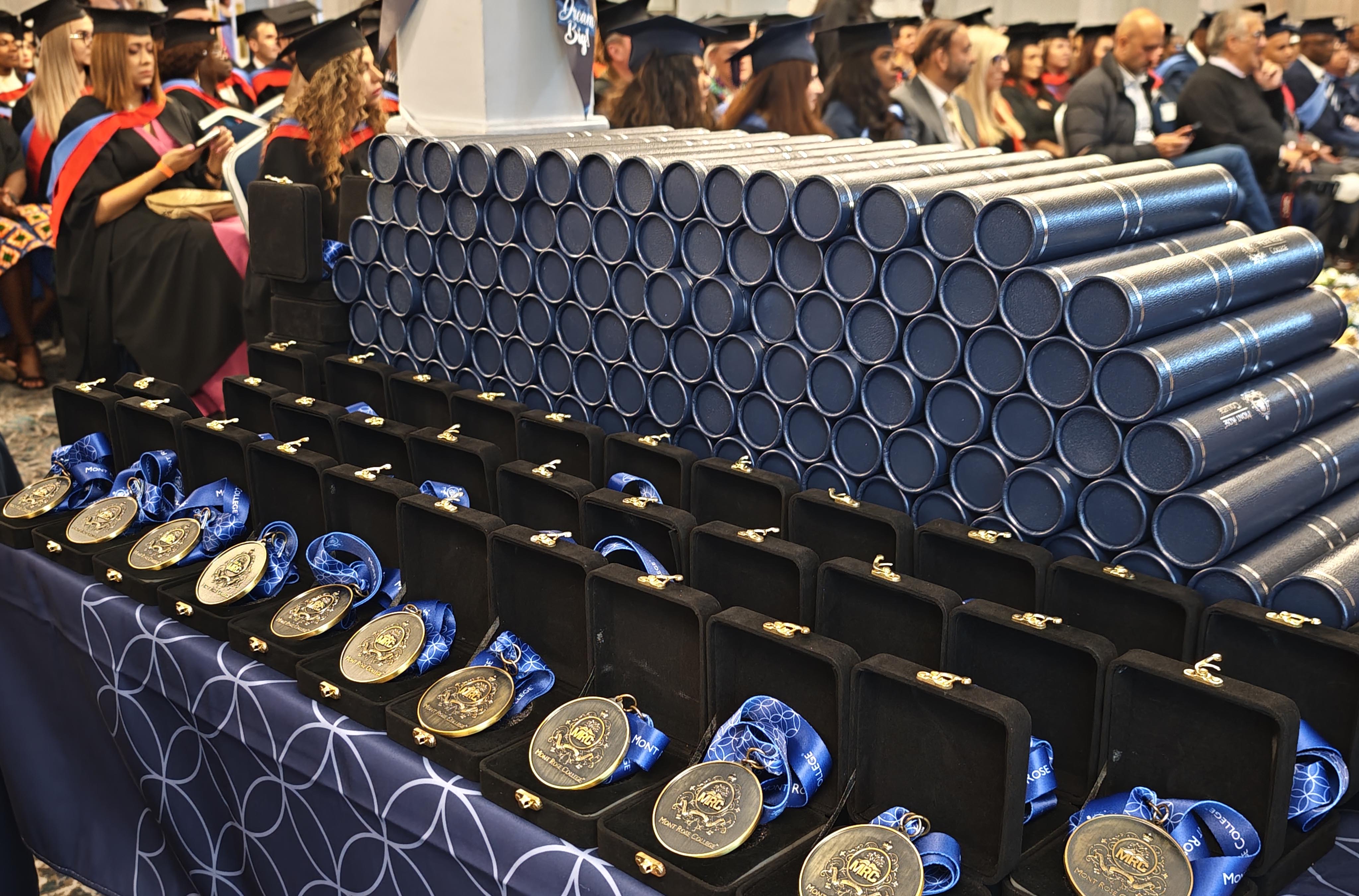 Close-up view of medals and diploma tubes displayed at Mont Rose College Graduation Ceremony 2024, with graduates seated.