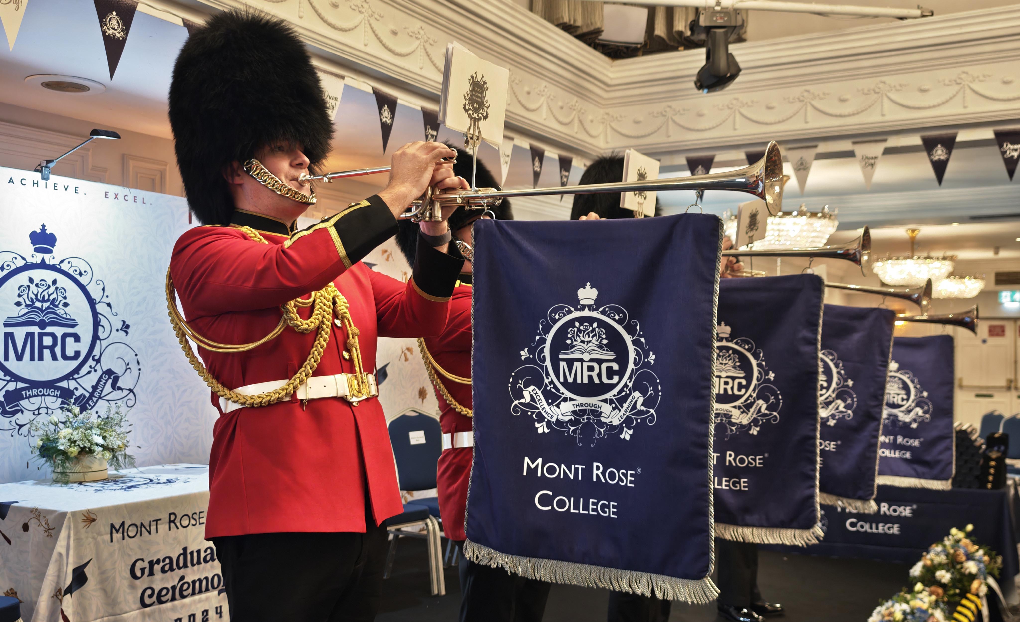 Uniformed guards in traditional red attire play ceremonial trumpets adorned with Mont Rose College banners at the Mont Rose College Graduation Ceremony 2024.