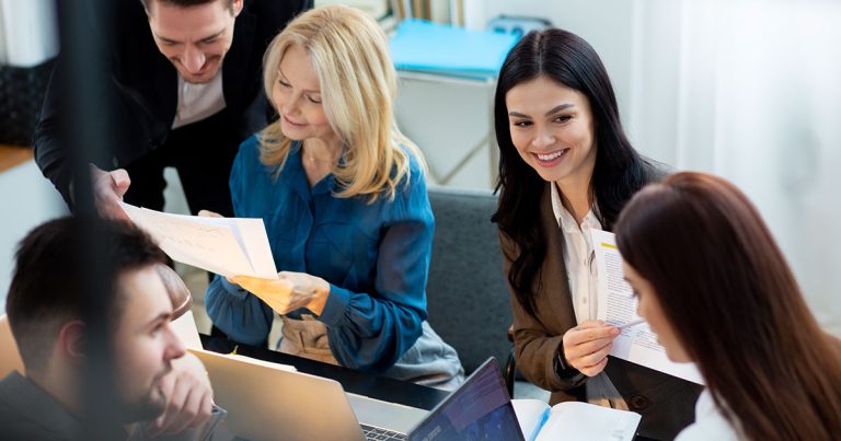 A group of professionals discussing documents and laptops, highlighting collaboration for Higher National Diplomas programs.