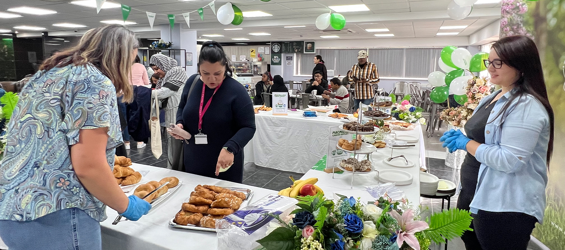 A vibrant setup at the Macmillan Coffee Morning at Mont Rose College, featuring guests selecting pastries and a beautifully decorated table with balloons and flowers.