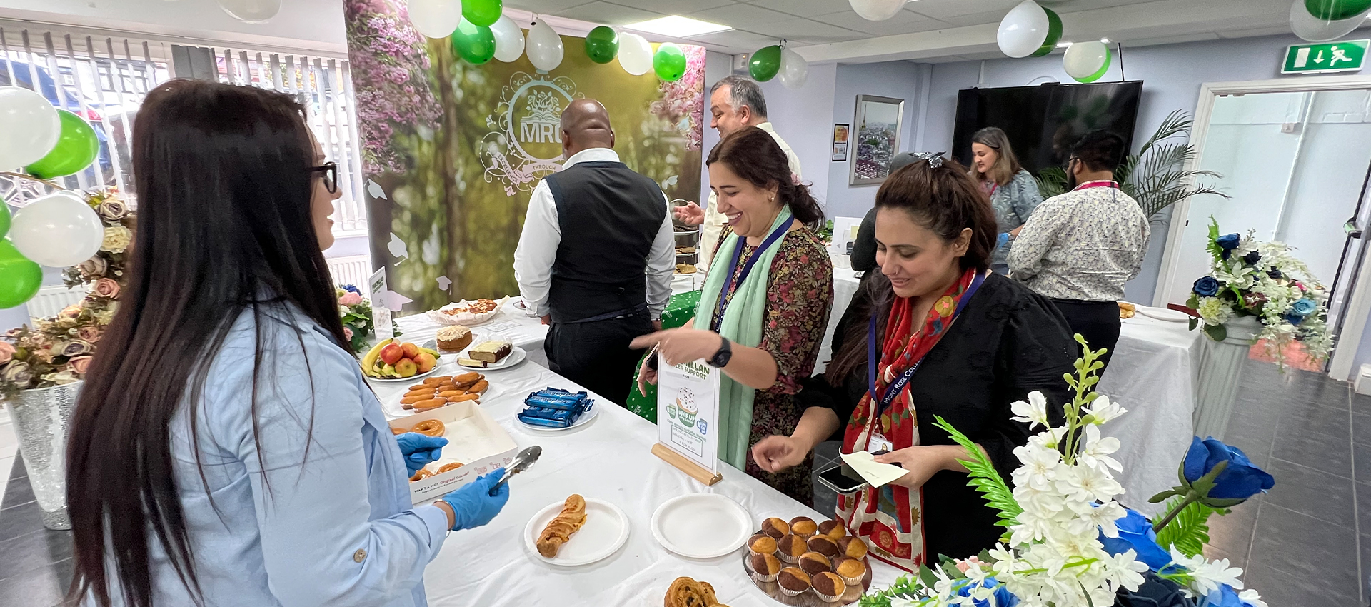 Guests enjoying treats and conversations at the Macmillan Coffee Morning at Mont Rose College, with a table filled with pastries, fruits, and desserts.