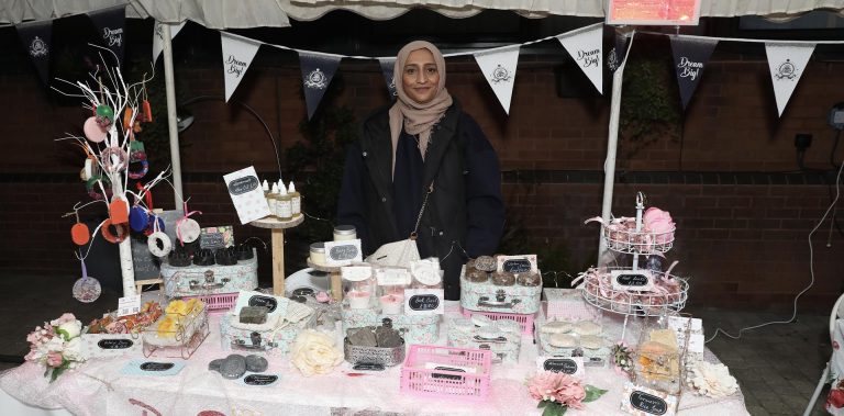 A festive stall displaying handmade soaps and gifts at a Christmas Cheer event, with a smiling vendor.