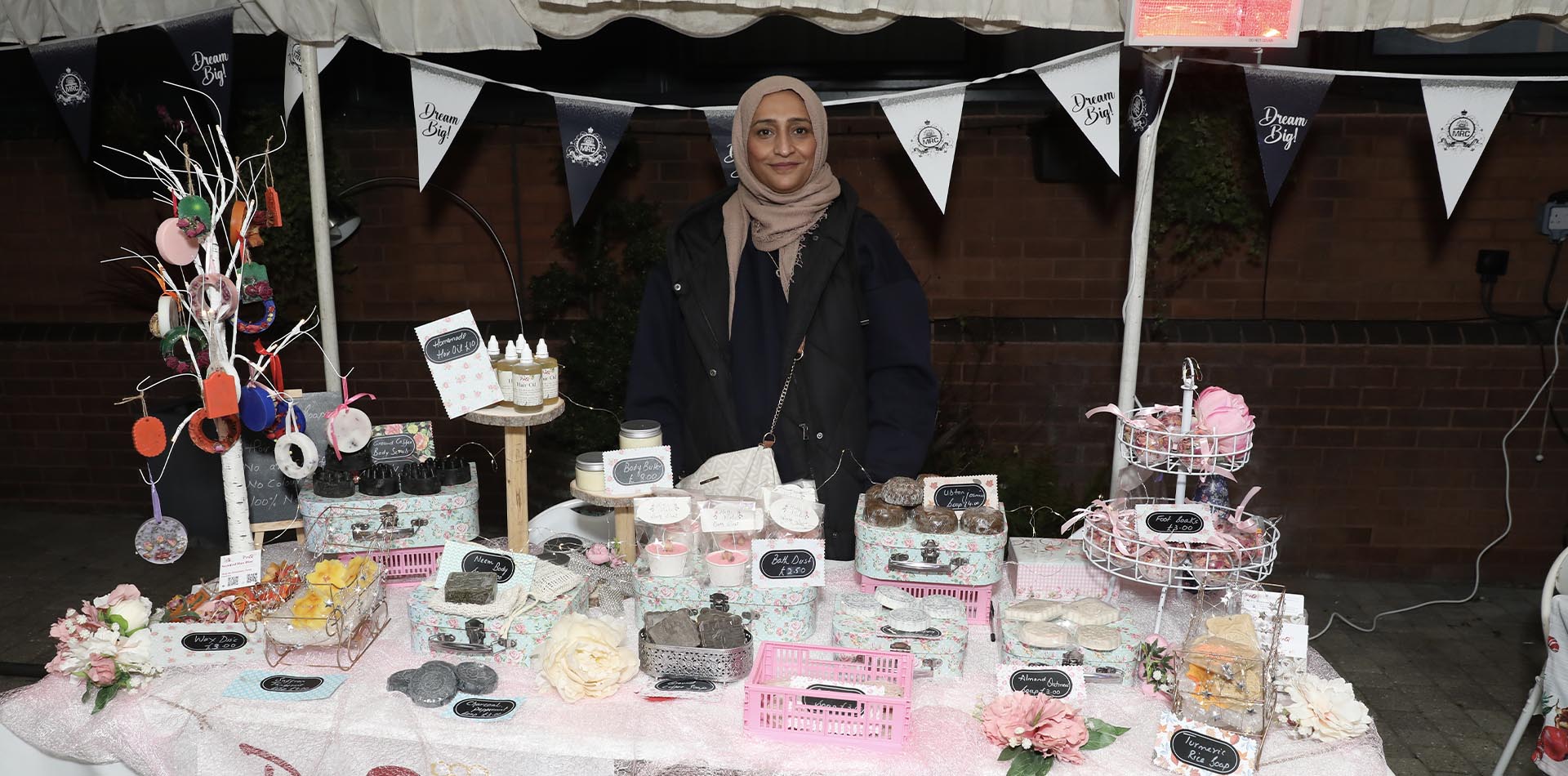 A festive stall displaying handmade soaps and gifts at a Christmas Cheer event, with a smiling vendor.