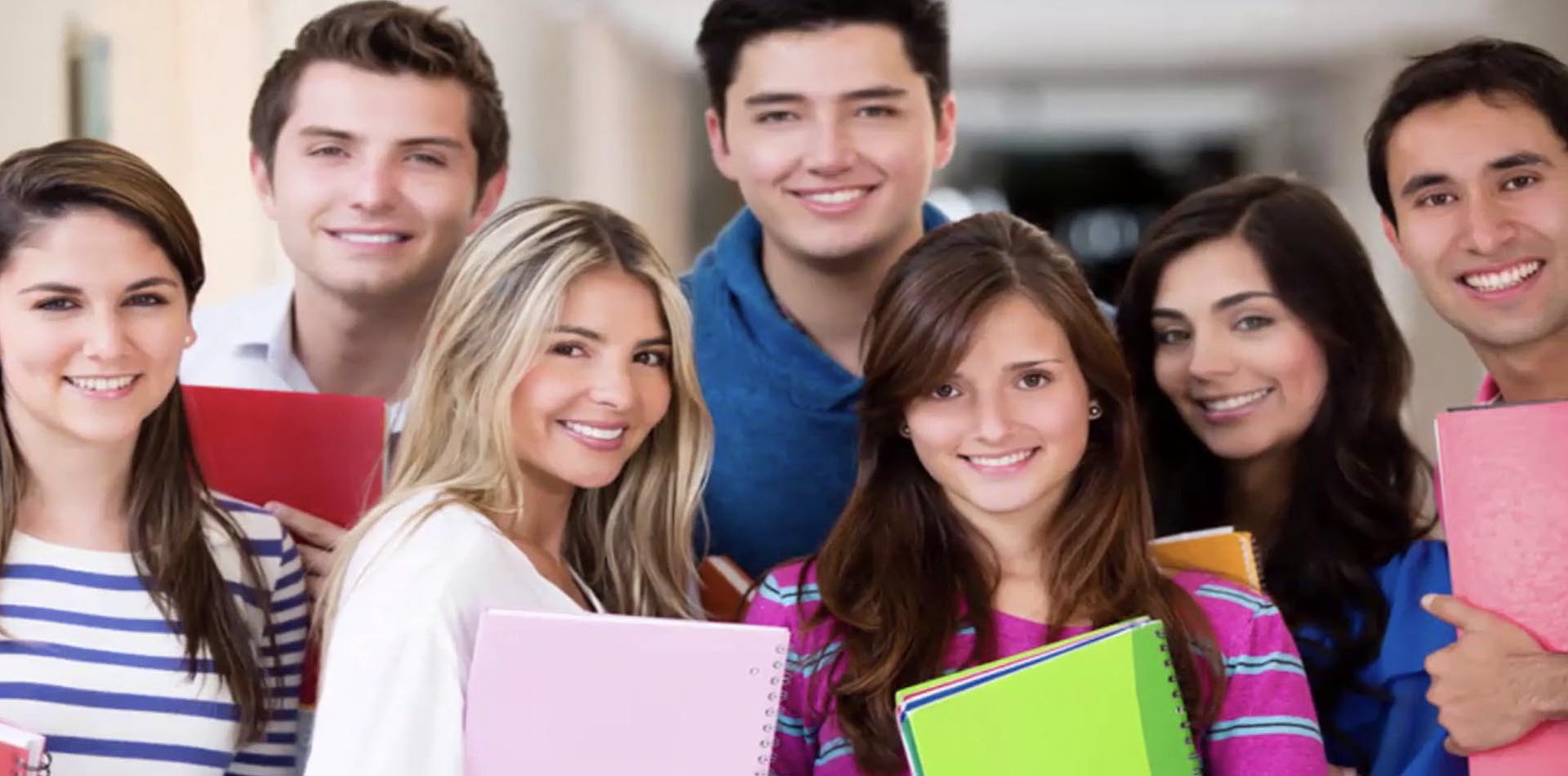 A group of smiling young adults holding colorful notebooks, representing students or professionals discussing educational paths such as HNDs vs Apprenticeships.