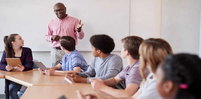 A teacher in a pink shirt engaging with a diverse group of students seated in a classroom, illustrating a discussion on the Global Recognition of HND Qualifications.