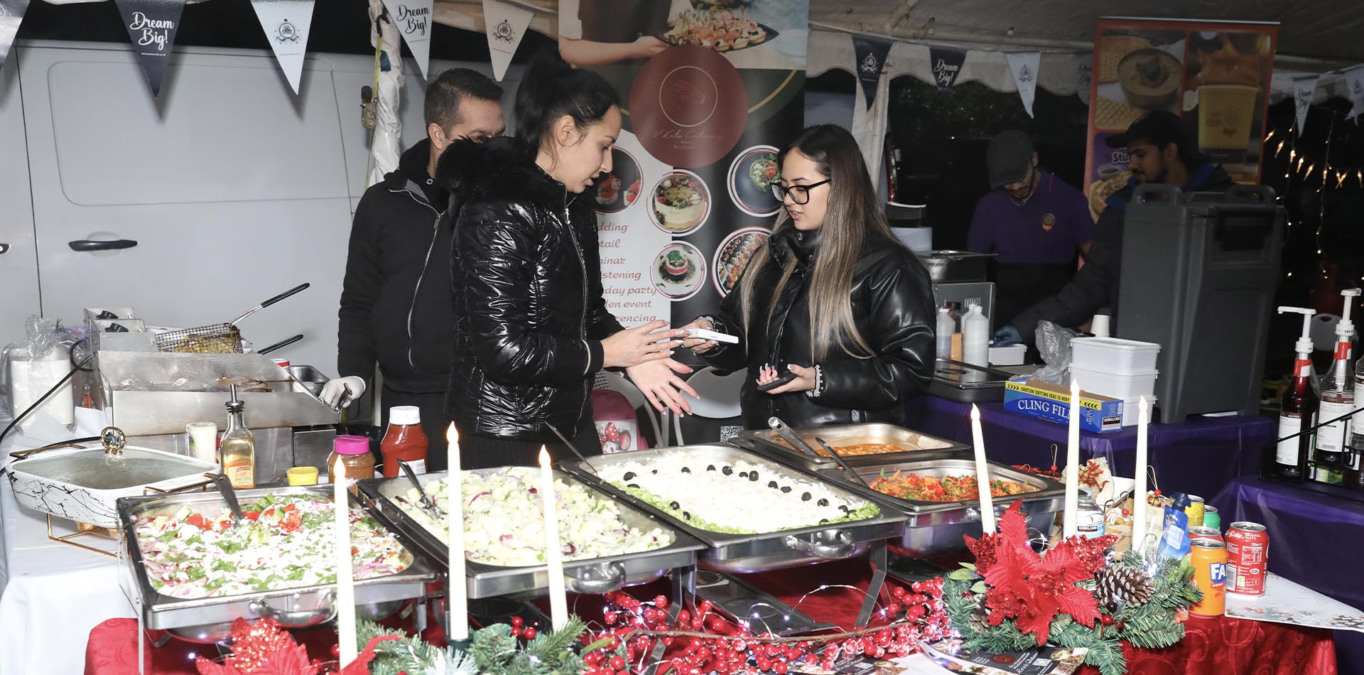 Festive food stall with colorful dishes, Christmas-themed decor, and friendly interaction, spreading Christmas Cheer in a lively, holiday atmosphere.