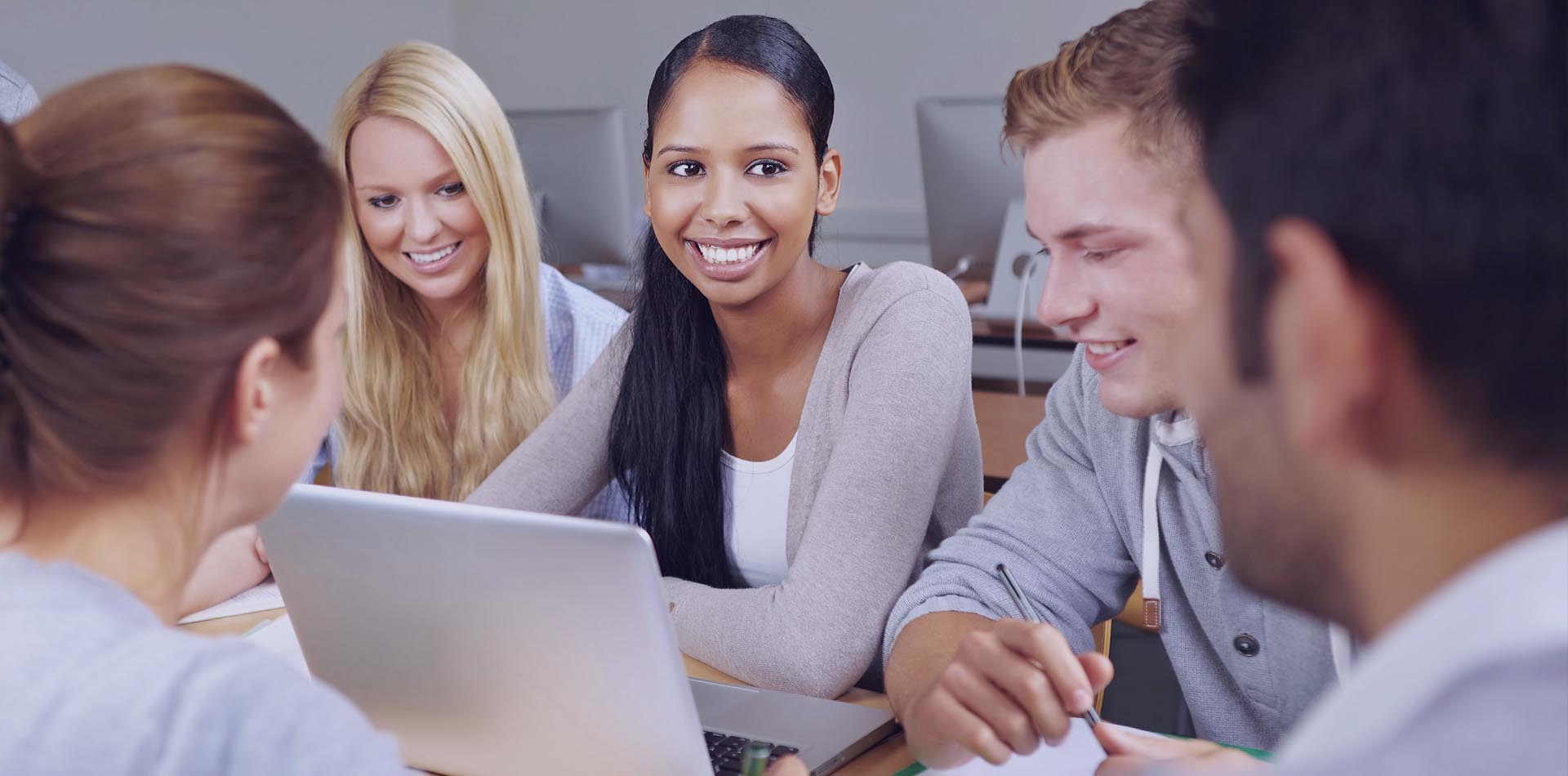 Group of students collaborating in a classroom setting, smiling and working together on a laptop, showcasing the Importance of Accreditation for HNDs in fostering teamwork and academic success.