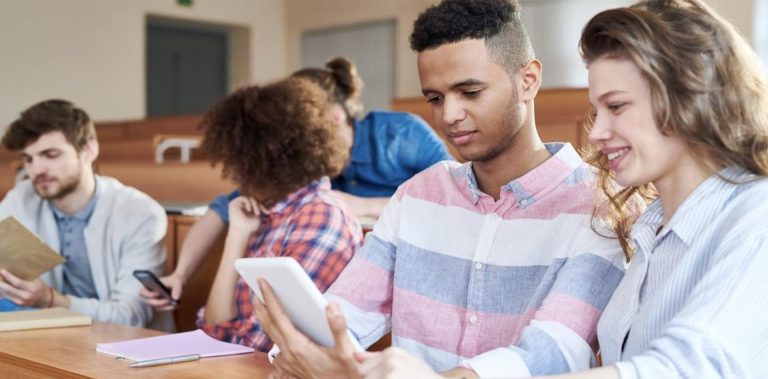 Students collaborating in a classroom setting, using a tablet to discuss learning opportunities, highlighting pathways like HNDs vs Apprenticeships for career advancement.