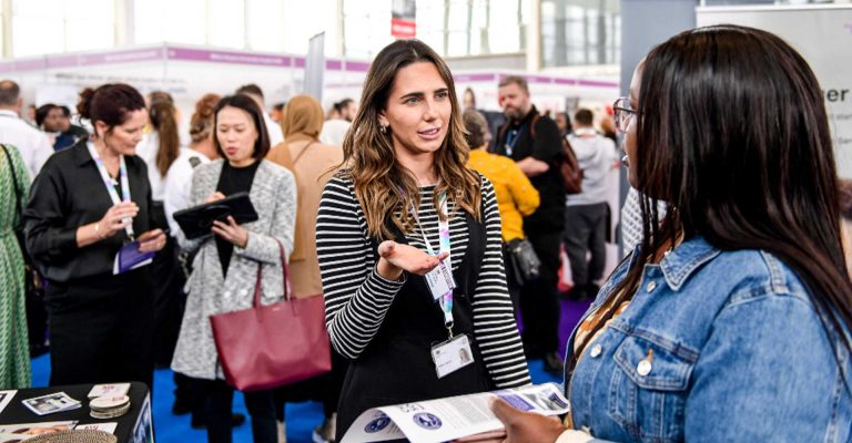 Two women conversing during the Stepping Into Opportunity – London Job Fair at Westfield Stratford, surrounded by attendees and booths.
