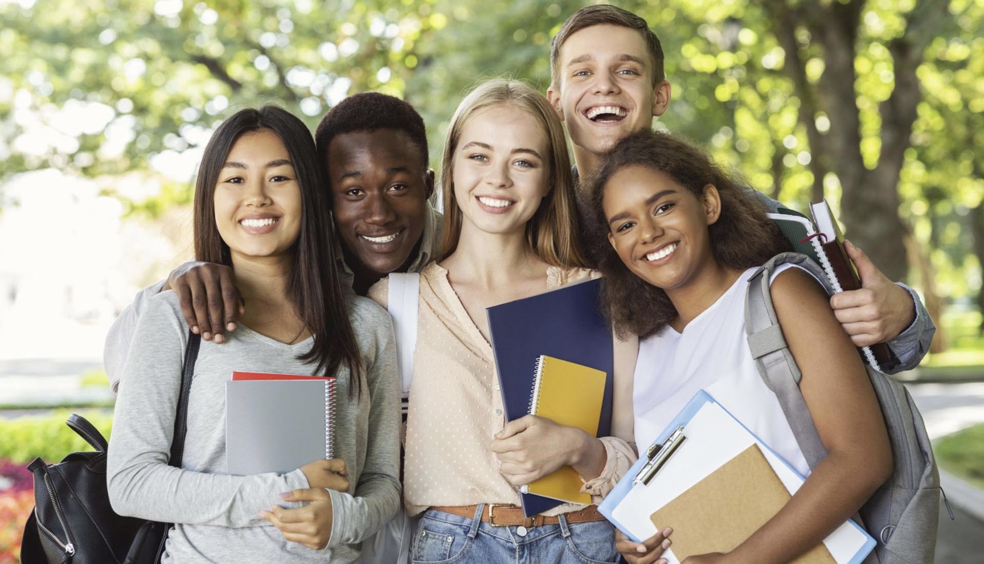 A diverse group of happy students holding books and notebooks outdoors, representing academic success in an HND Course.