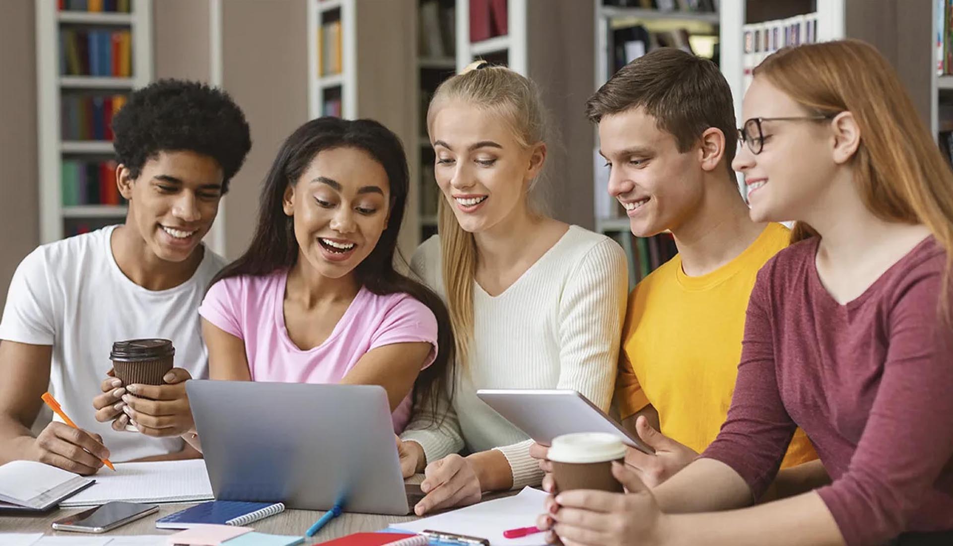 A diverse group of students collaborating on a project during their HND Course, using a laptop and taking notes in a library.
