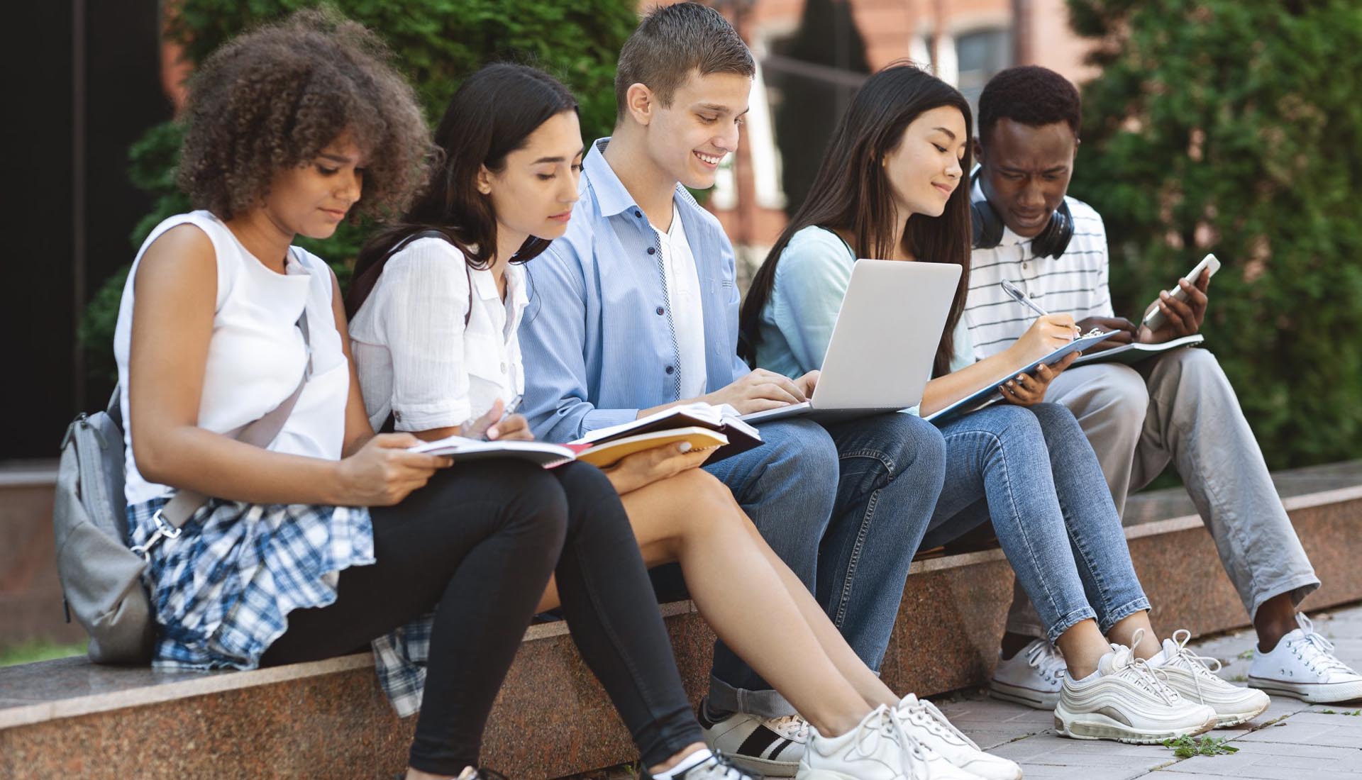 A diverse group of students studying outdoors with books and a laptop, representing collaborative learning in HND Programs.