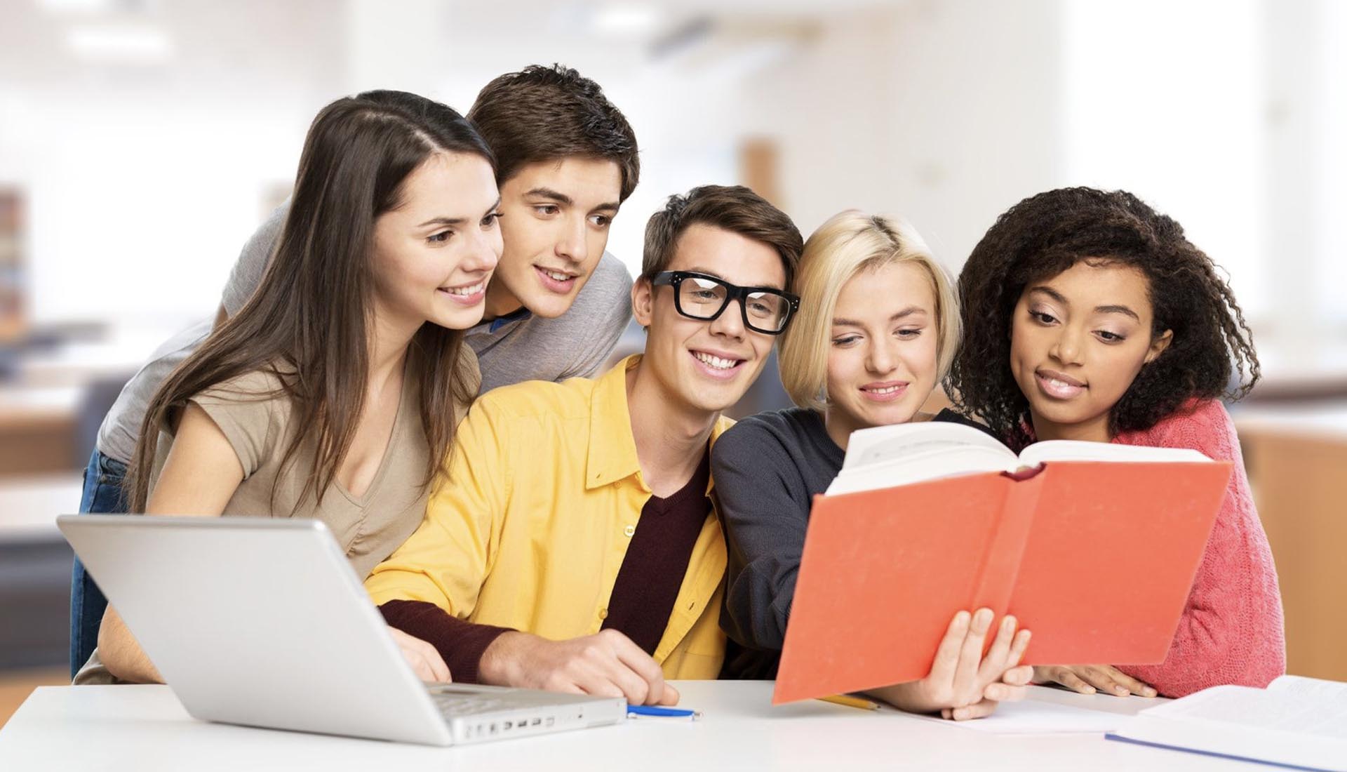 A diverse group of students studying together with a book and laptop, representing collaboration in HND Programs.