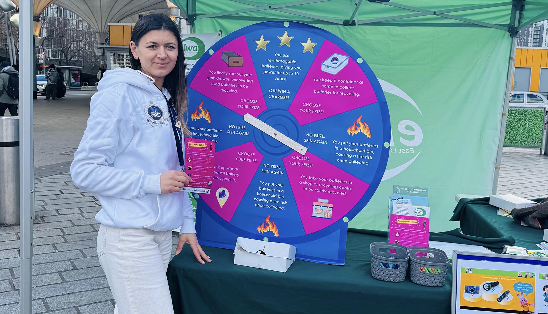 A Mont Rose College representative at the National Battery Day Awareness Event, promoting battery recycling with an interactive spin-the-wheel game.