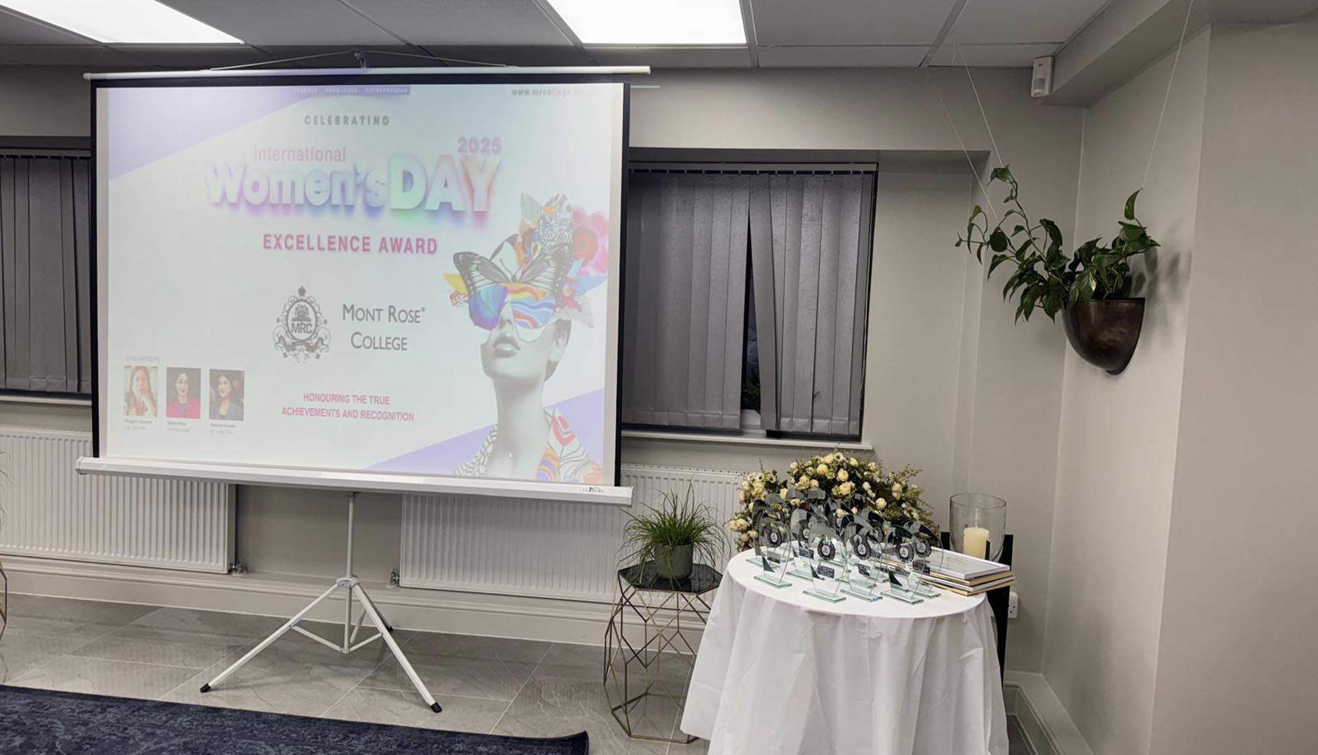A projector screen and award table set up for Celebrating International Women’s Day at Mont Rose College, honoring achievements and recognition.