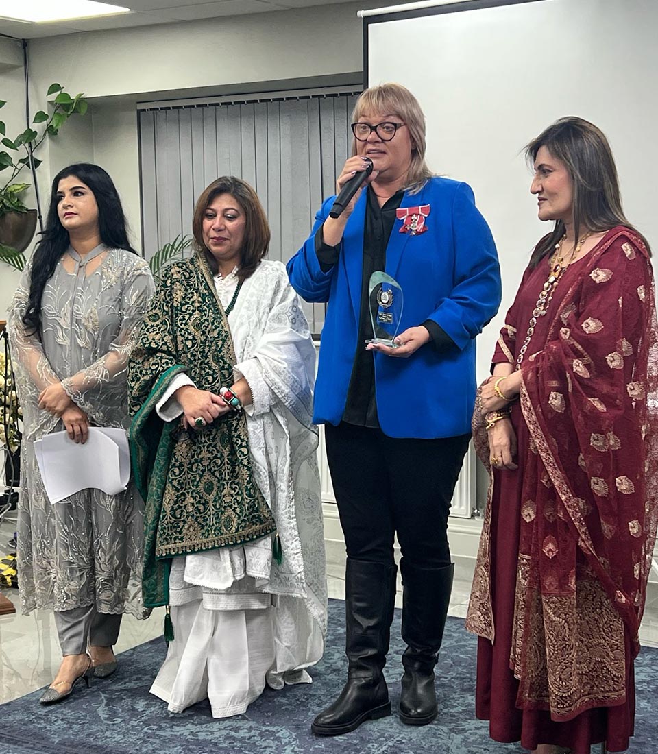 A woman in a blue blazer holds an award and speaks at Celebrating International Women's Day at Mont Rose College, honoring women's achievements.