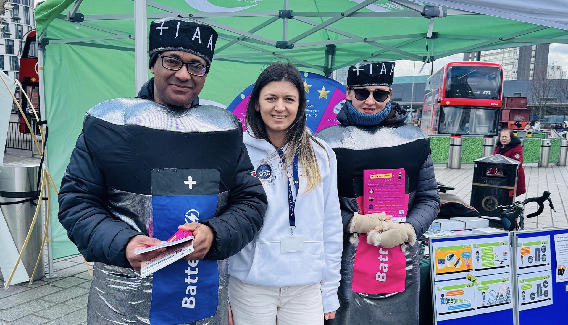Three participants, including two dressed as batteries, promoting recycling at the National Battery Day Awareness Event.