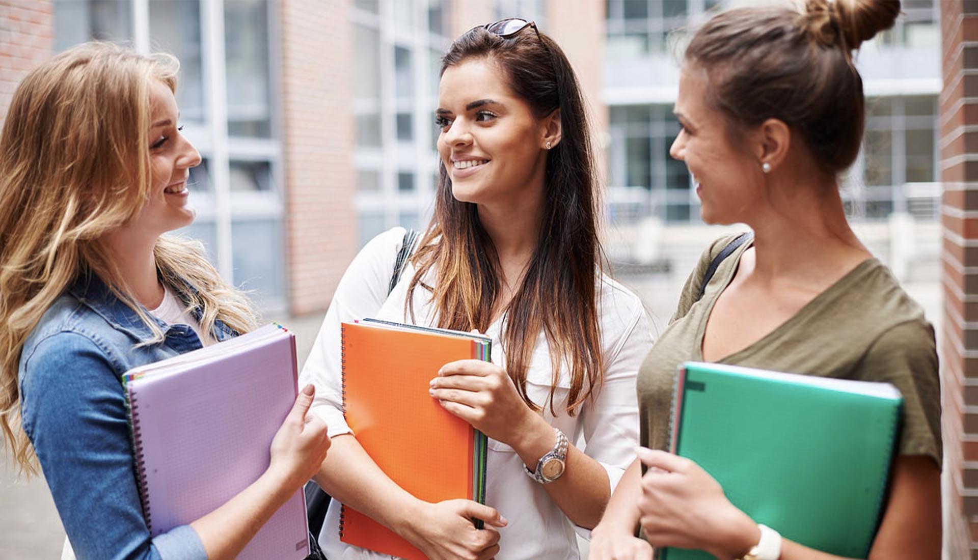 Three smiling students holding notebooks, discussing their studies, highlighting the benefits of HND Qualifications for career growth.