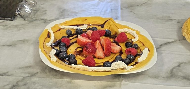 A delicious pancake decorated with strawberries, raspberries, blueberries, whipped cream, and chocolate drizzle for Pancake Day celebrations.
