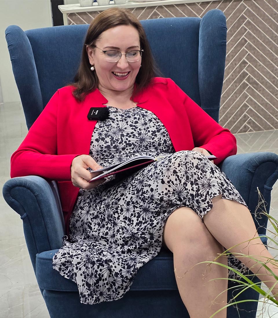 A woman in a red blazer joyfully reading a book while seated in a cozy chair, celebrating World Book Day.