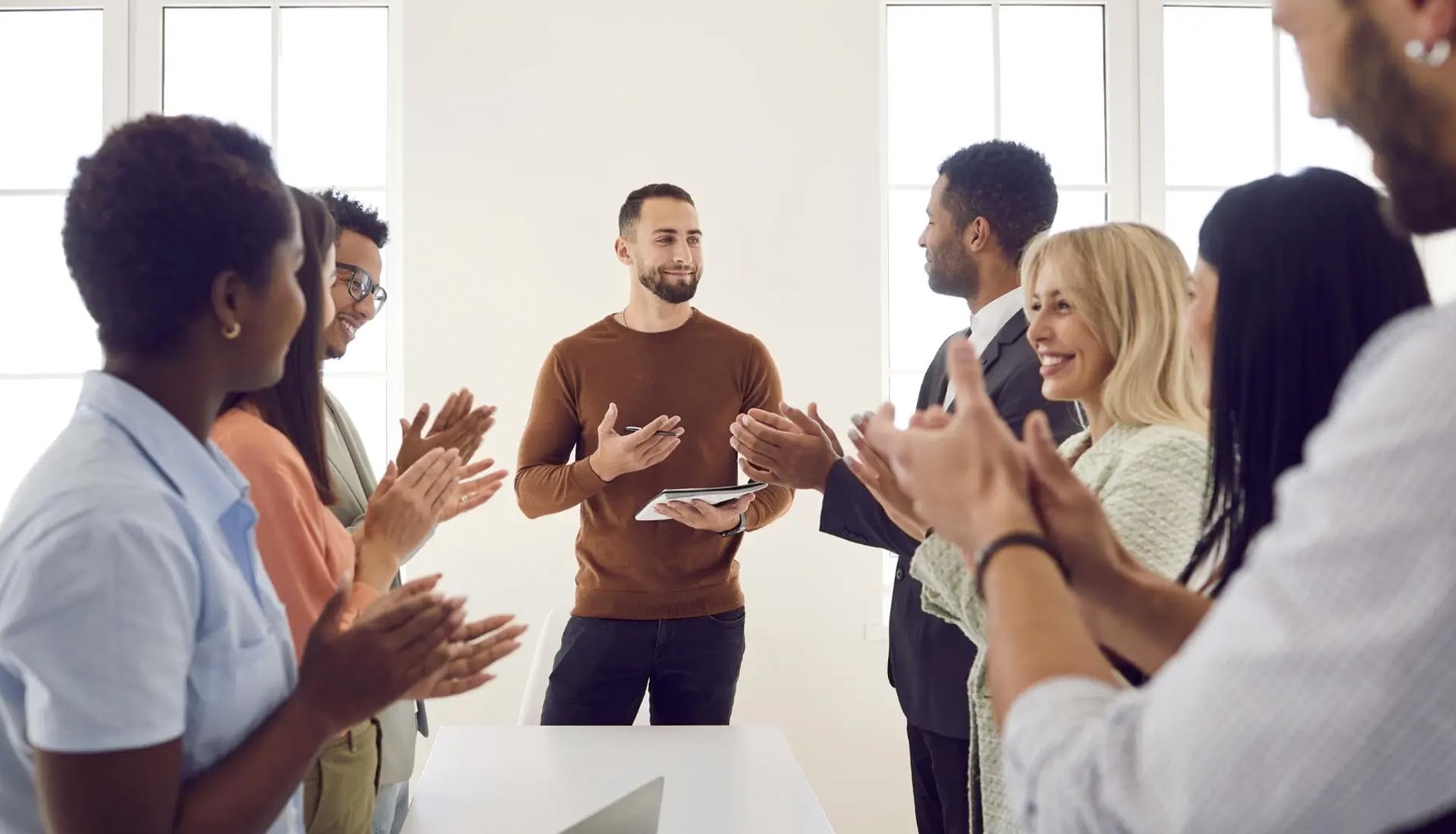 Group applauding a man with a tablet in a bright room, symbolizing success in HNDs and Entrepreneurship.