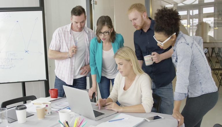 Students collaborating around a laptop during a group project, illustrating Networking in an HND Programme.