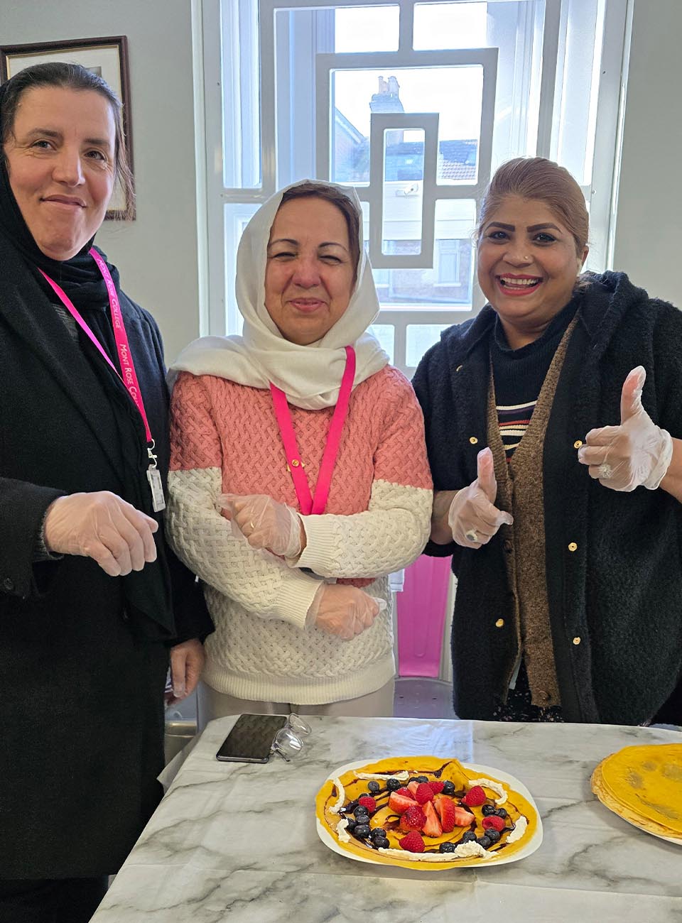 Three women smiling and posing with a decorated pancake topped with fruit during a Pancake Day celebration at Mont Rose College.