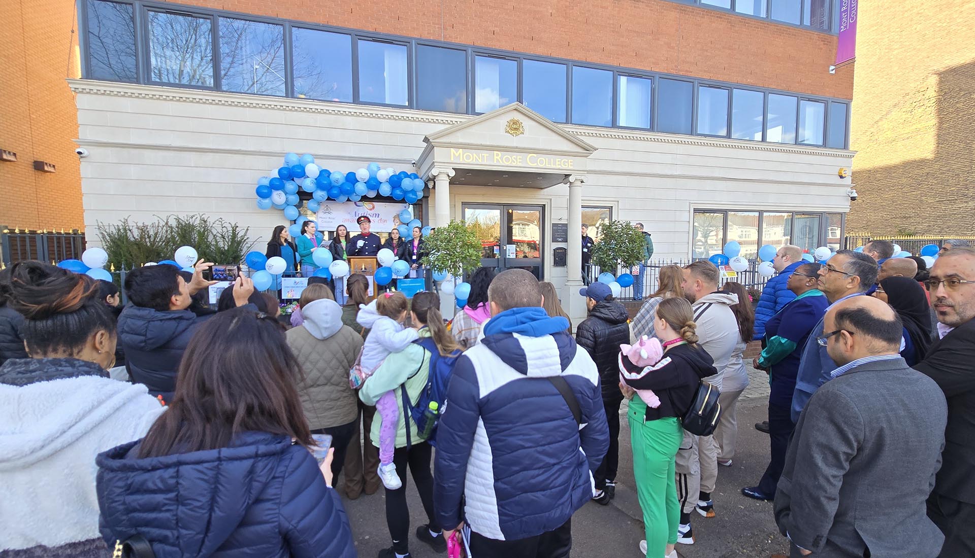 Crowd gathers outside Mont Rose College for speeches during the inspiring Autism Awareness Event decorated with blue balloons.
