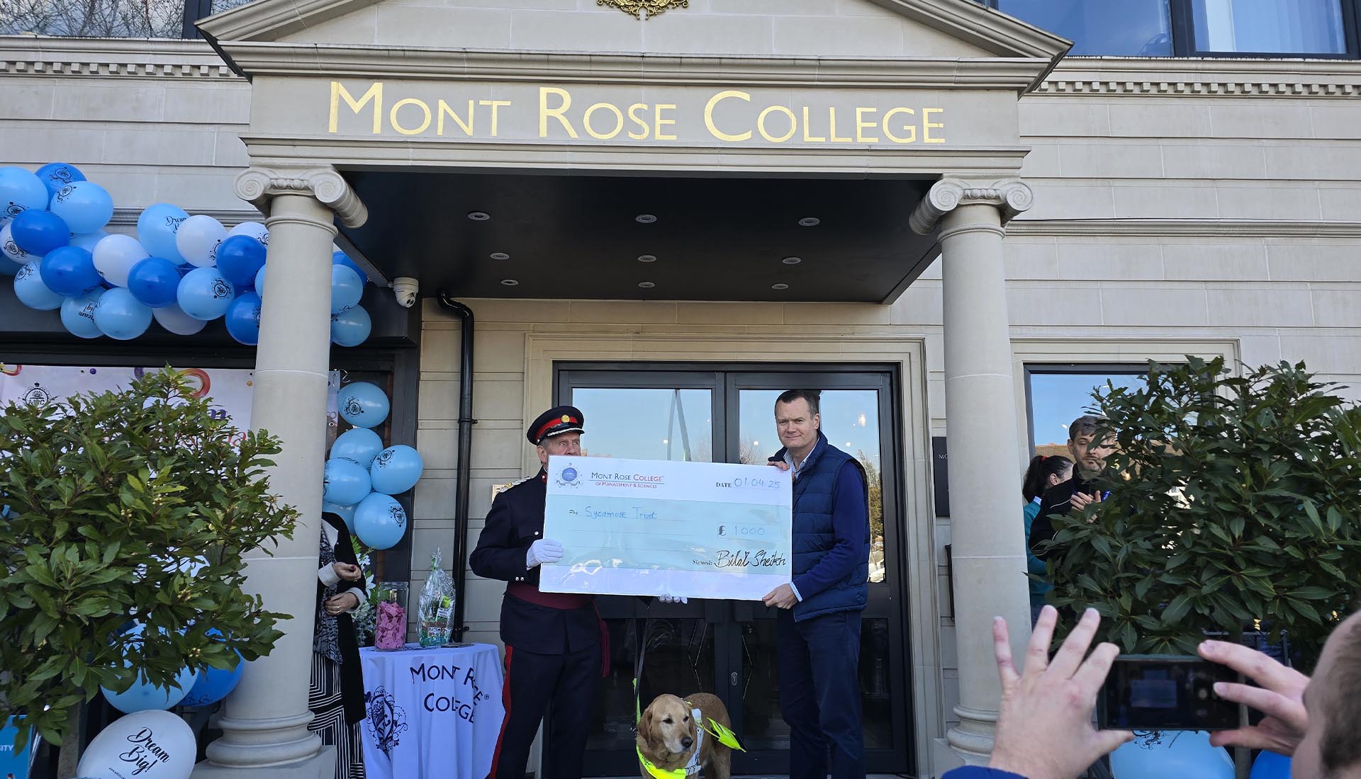 Two men present a donation cheque outside Mont Rose College during its inspiring Autism Awareness Event.