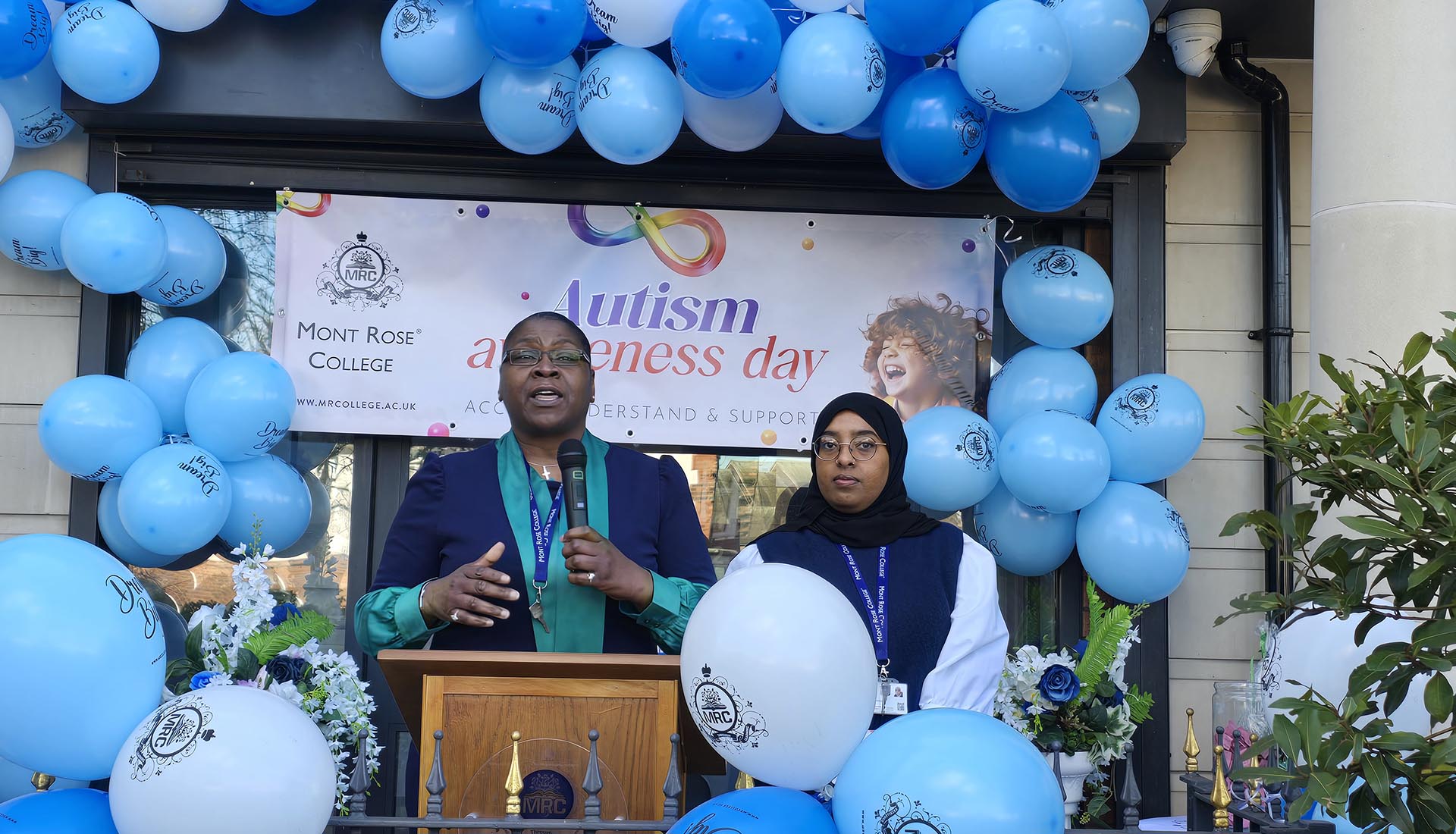 Two speakers address the crowd at Mont Rose College’s inspiring Autism Awareness Event, surrounded by blue balloons.