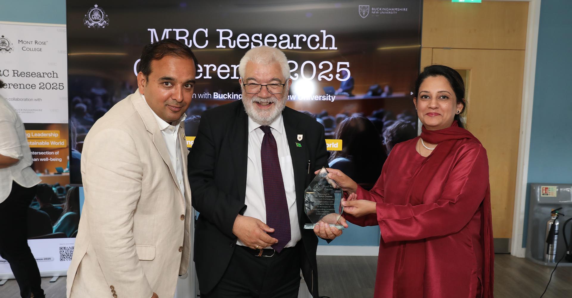 Award presentation during the MRC Research Conference 2025, with attendees smiling in front of the event backdrop.