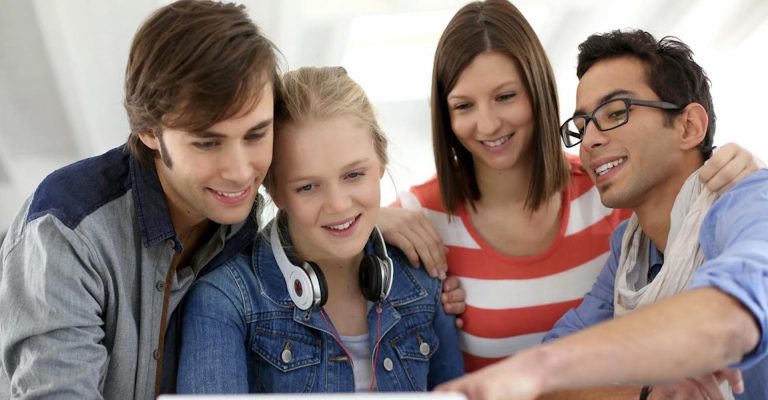 Group of students smiling and looking at a laptop, illustrating HND vs. Associate Degrees educational comparison.