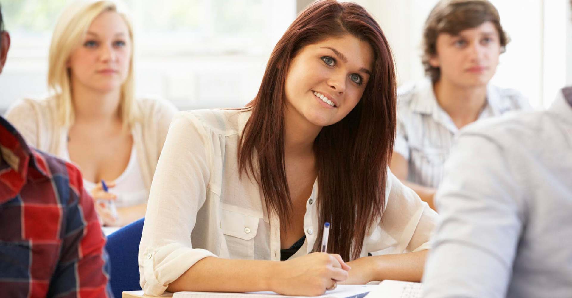 Smiling student taking notes in class, illustrating the comparison between HND vs Online Certifications for career advancement.