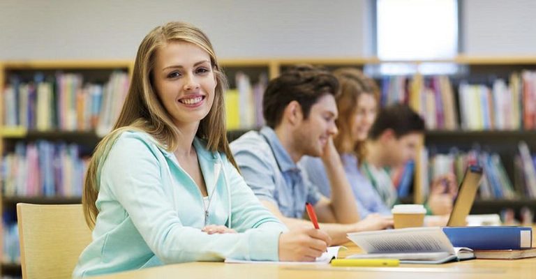 Smiling student writing in library, symbolizing the comparison of HND vs Online Certifications in academic settings.