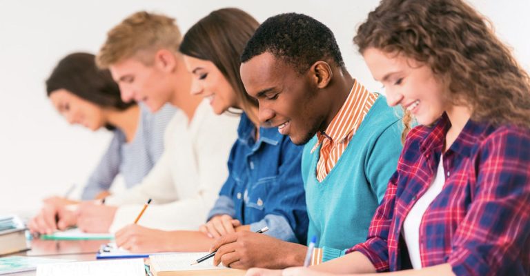 Smiling students writing in class, representing academic comparison of HND vs Higher Education Diplomas options.