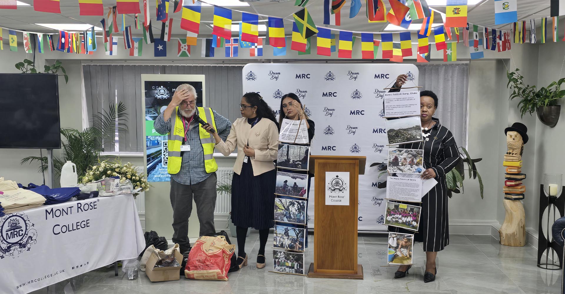 Speakers presenting posters and materials at Mont Rose College during an Environment Day Programme event under international flags.