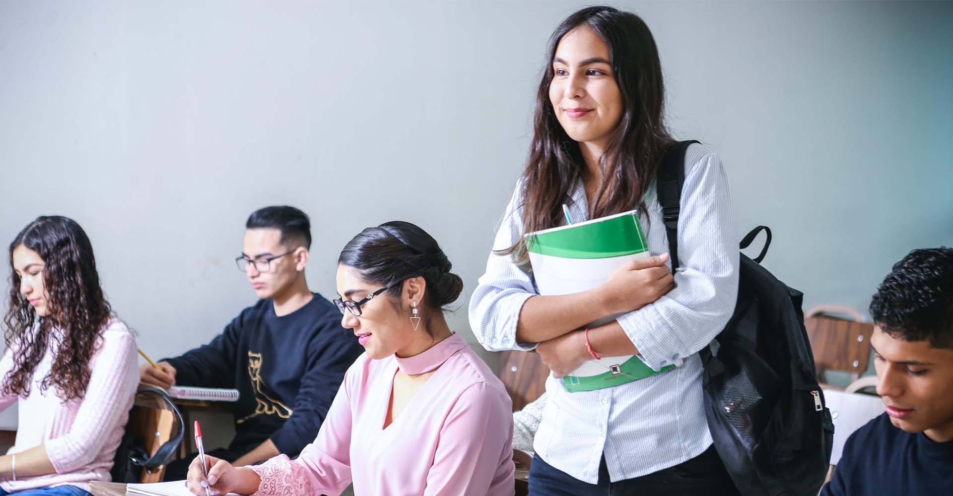 Student standing with notebooks in a classroom, highlighting educational decisions like HND vs Professional Qualifications.