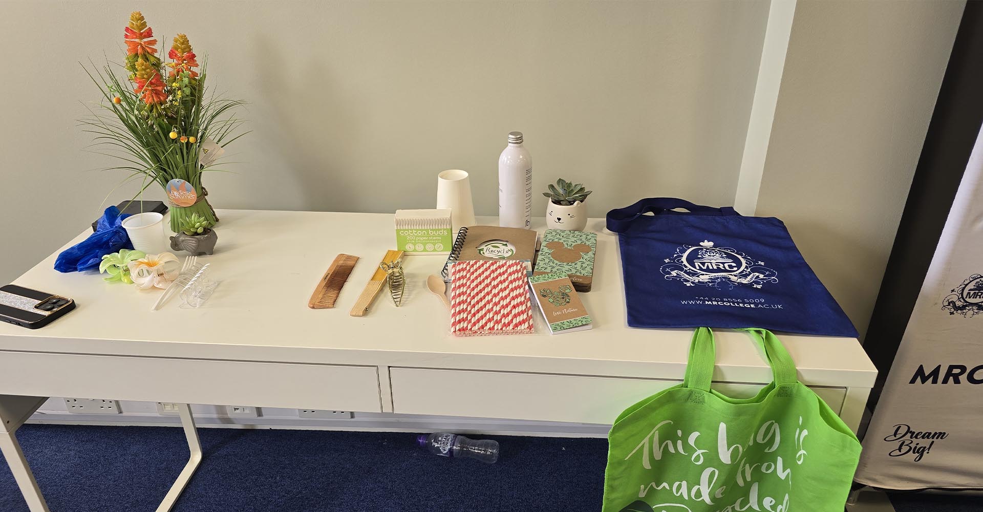 Table display of eco-friendly items like reusable bags, notebooks, and bamboo utensils for Environment Day at Mont Rose College.